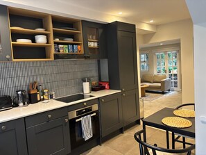 A modern kitchen with dark cabinetry, a tiled backsplash, and a dining area with a table and chairs. - Elegant St Johns Wood Mews-king Bed Workspace (London)