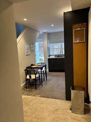 A kitchen with dark cabinets, a window, and a dining area with a table and chairs. - Elegant St Johns Wood Mews-king Bed Workspace (London)
