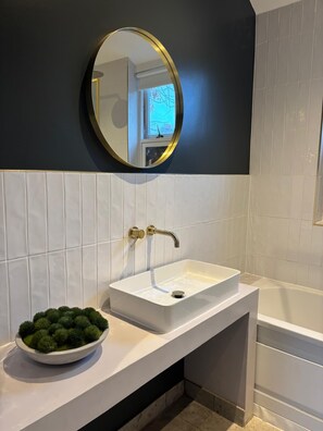 A bathroom with a white sink, a round mirror with a gold frame, and a bathtub. - Elegant St Johns Wood Mews-king Bed Workspace (London)