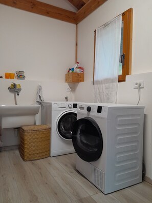 Een wasserette met een wasmachine, een wasbak en een houten plank met toiletartikelen.