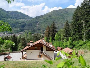 Een chalet met schuin dak, een balkon en uitzicht op een vallei met bergen op de achtergrond.