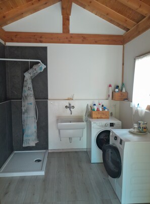 Une buanderie équipée d’un lave-linge, d’un évier et d’un espace douche.