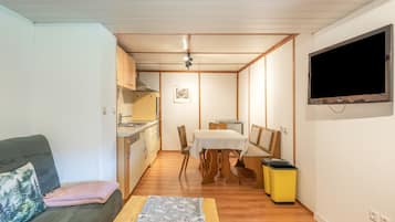 A compact living space with a kitchenette, a dining area, a sofa, and a TV mounted on the wall.