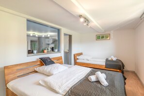 Een hotelkamer met twee houten bedden, een spiegel, een kleine kitchenette en een ingelijste foto aan de muur.
