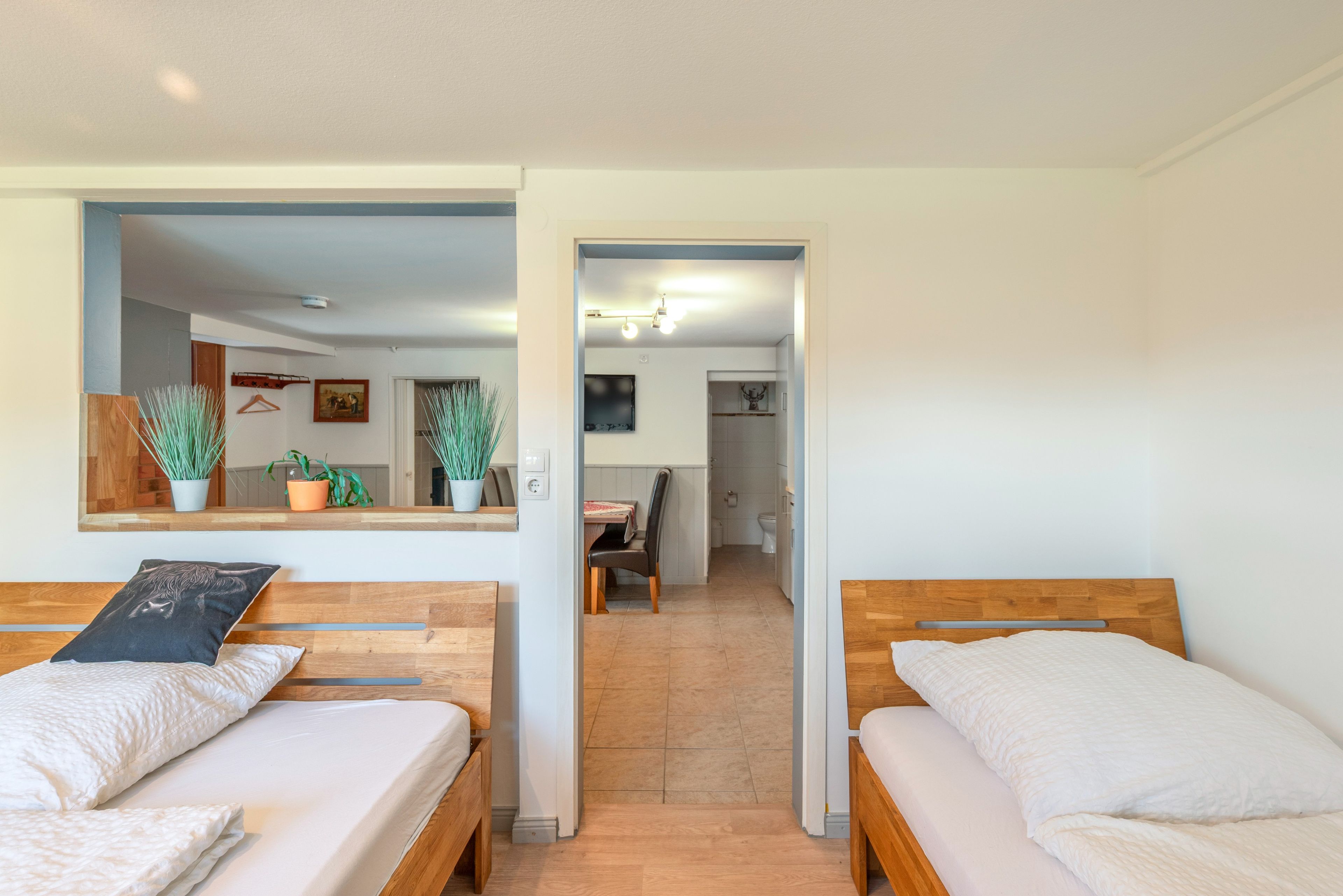 A room with two wooden beds, a mirror, and a view into a dining area.