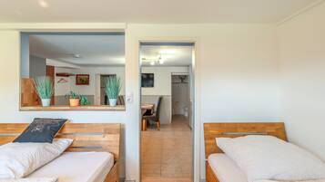 A room with two wooden beds, a mirror, and a view into a dining area.