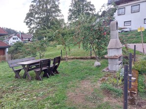 Ein Sitzbereich im Freien mit einem Picknicktisch und Stühlen, umgeben von Gras und Bäumen.