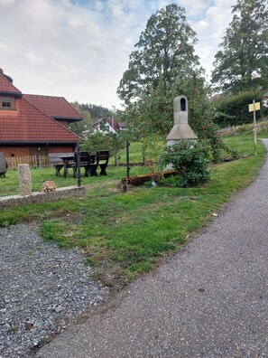 Ländliche Umgebung mit einem Steinbau, Holzbanken und einem Kiesweg.