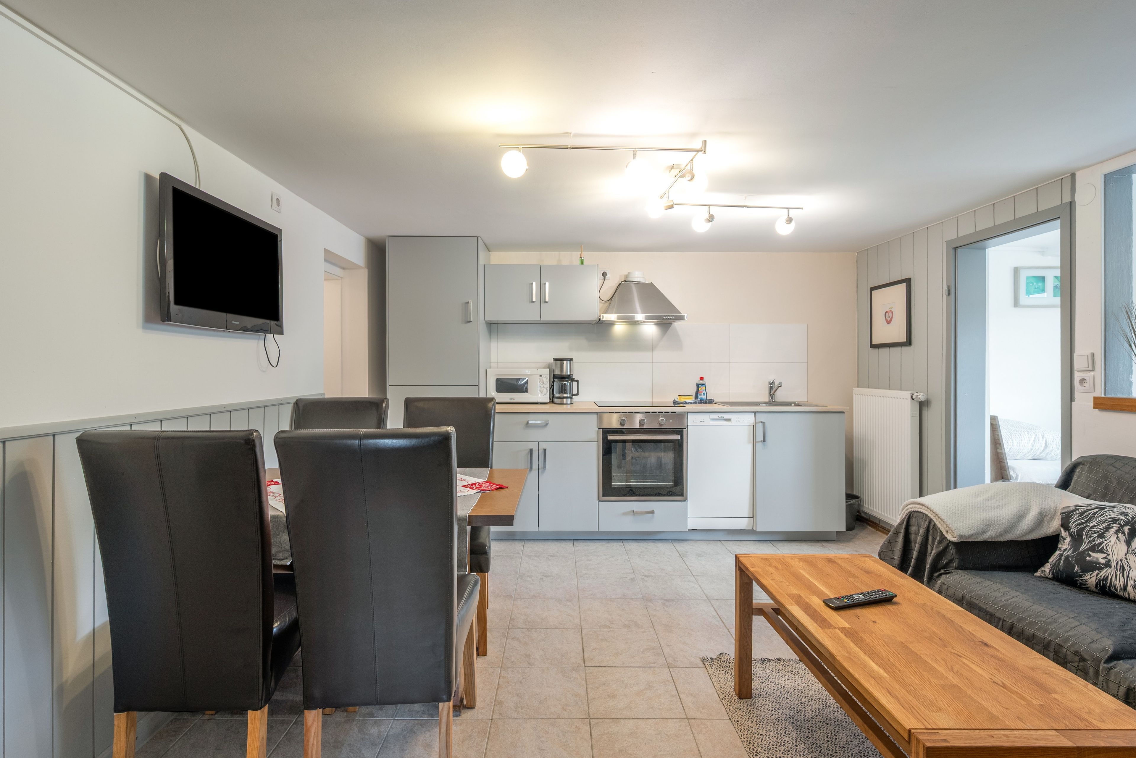 A modern kitchen with a dining area, a TV mounted on the wall, and a sofa in the living room.