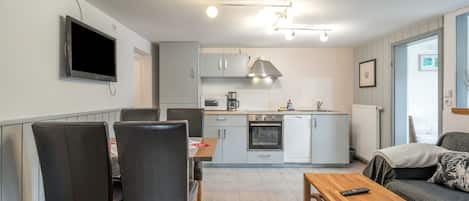 A modern kitchen with a dining area, a TV mounted on the wall, and a sofa in the living room.