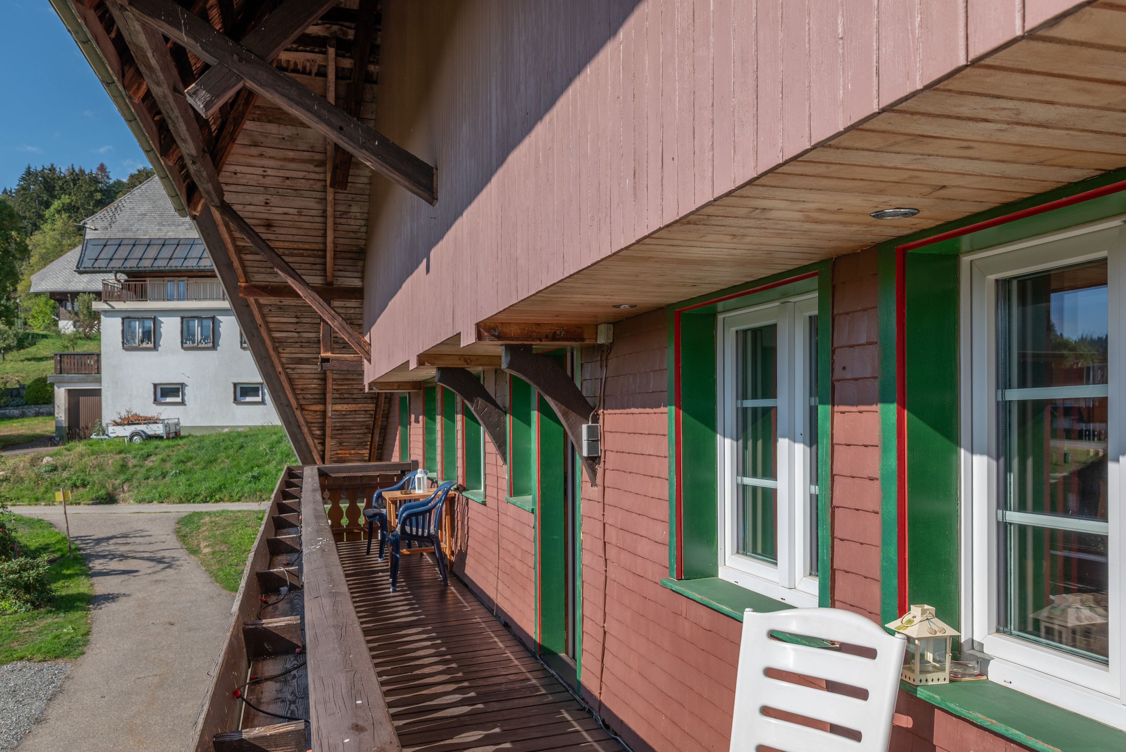 Ein Holzhaus mit Balkon, einem Fenster mit grüner Umrandung und einem Stuhl.