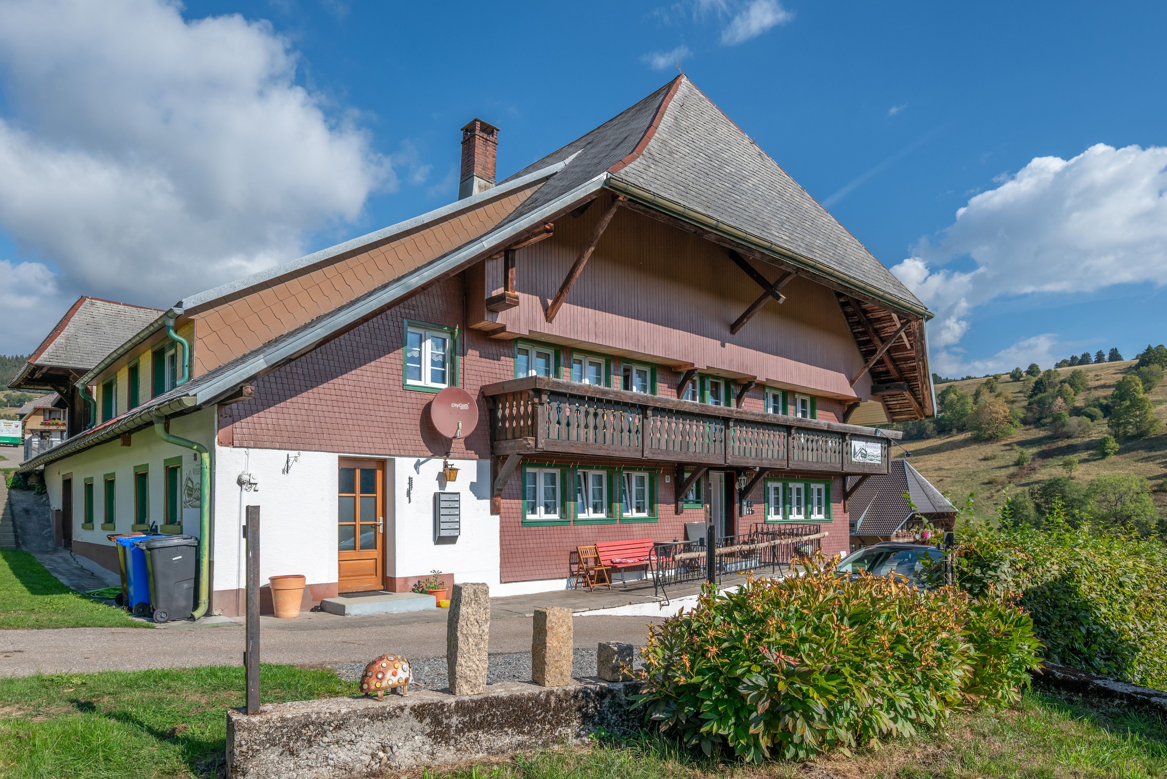 Ein traditionelles Chalet mit einem steilen Walmdach, hölzernen Balkonen und einer Veranda mit Sitzgelegenheiten.