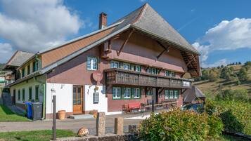 Ein traditionelles Chalet mit einem steilen Walmdach, hölzernen Balkonen und einer Veranda mit Sitzgelegenheiten.