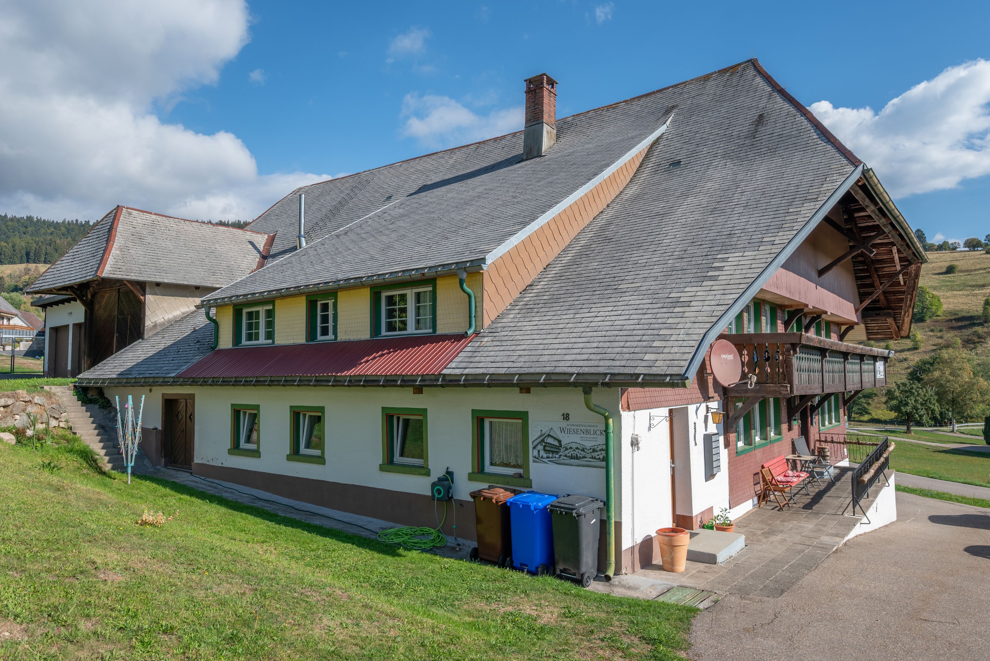 Ein traditionelles Chalet mit steilem Dach, Schornstein und einem Balkon mit Holzwerteln.
