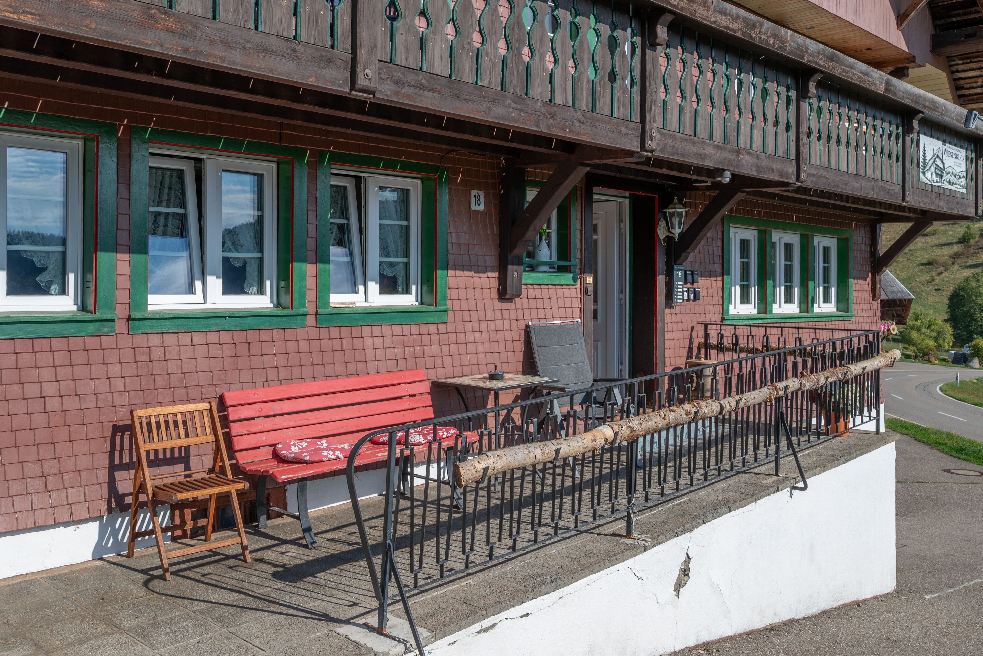 Ein traditionelles Chalet mit Holzbalkon, einer roten Bank und einem Tisch mit Stühlen.