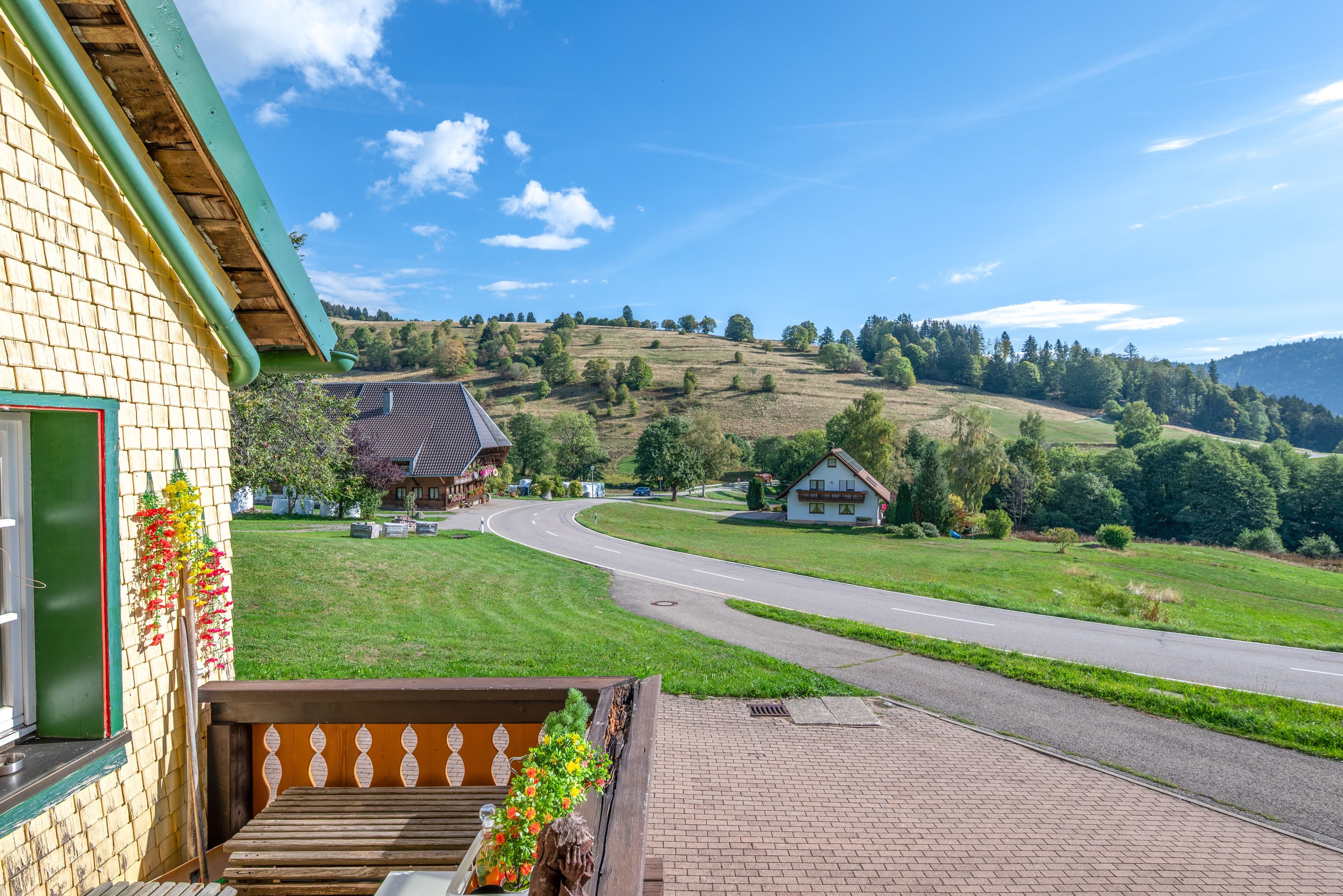 Ein Landweg führt zu einem Haus mit grüner Dachbegrünung, umgeben von viel Grün und Hügeln.