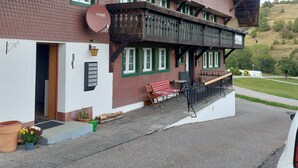 Un edificio de dos pisos con balcón, antena parabólica y un pequeño espacio de estar al aire libre.