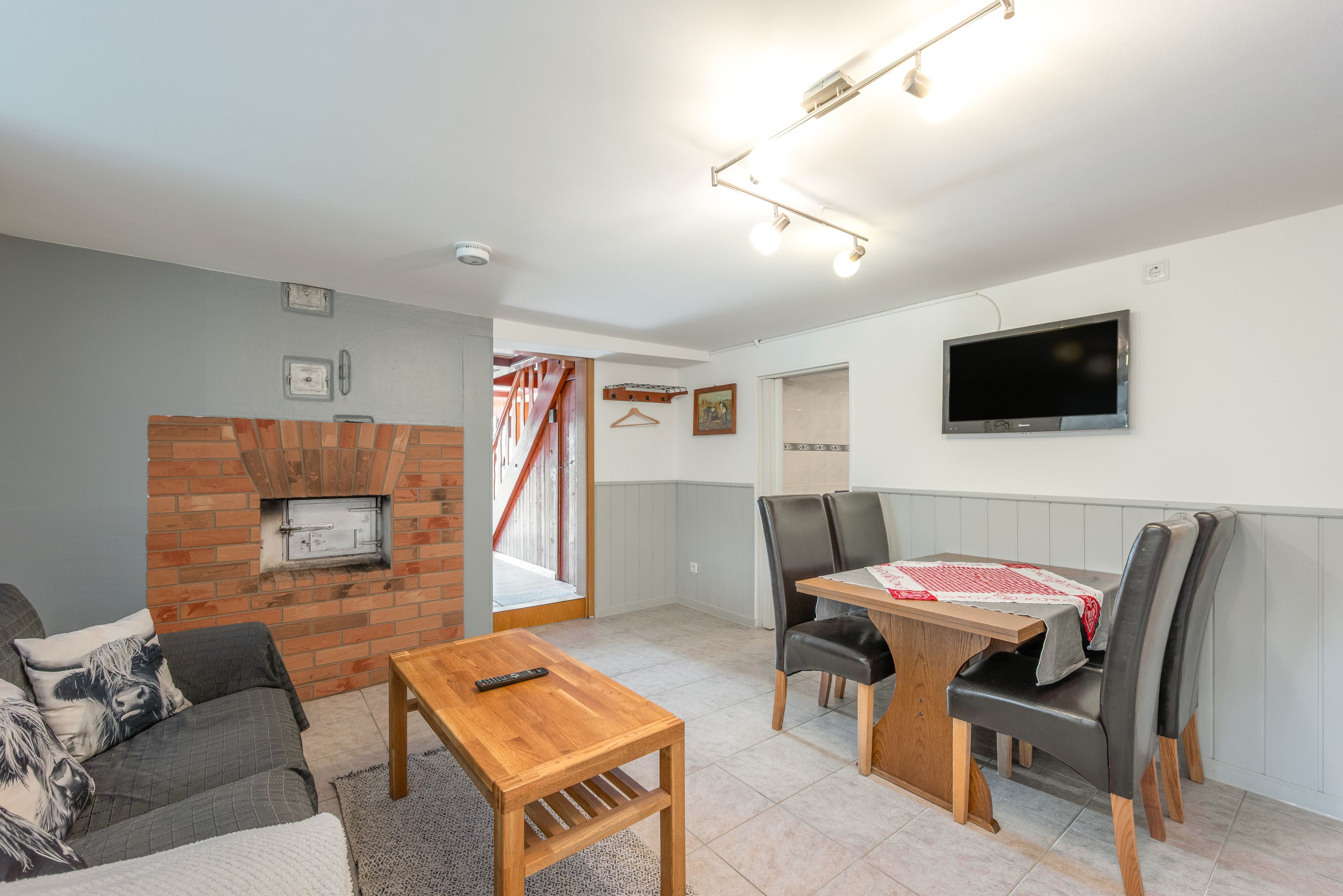 Ein Wohnzimmer mit Kamin, einem an der Wand montierten Fernseher, einem Esstisch mit Stühlen und einer Couch.
