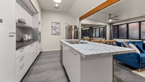 A modern kitchen with a marble island, stainless steel appliances, and a dining area with a blue sofa. - Private 2BR Villa | Minutes from Brisbane CBD (Spring Hill)