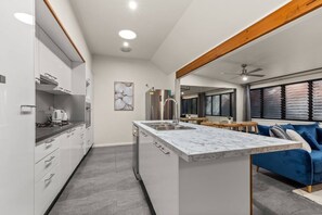 Cozinha moderna com ilha de mármore, eletrodomésticos de aço inoxidável e área de jantar com sofá azul.