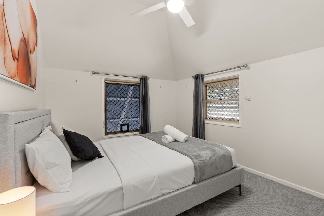 Una camera da letto con un letto, una finestra vista, una ventola a soffitto e un quadro appeso al muro.