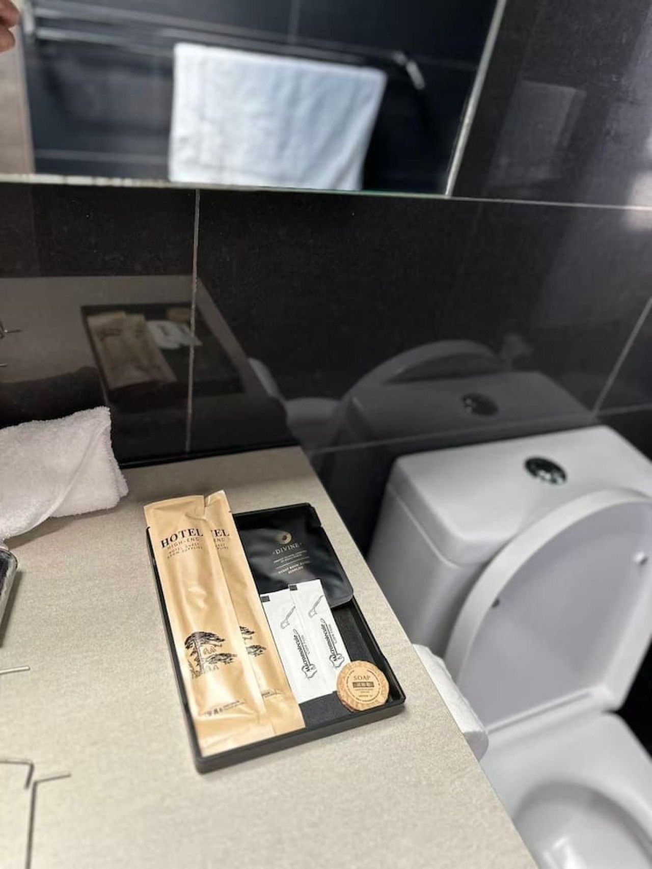 Casa de banho de hotel com bancada preta, toalha branca, dispensador de sabonete e bandeja com artigos de higiene pessoal.