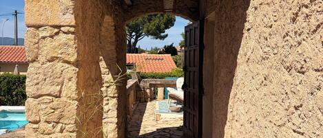 Un arco de piedra que da paso a una zona de piscina con un techo de azulejos a la vista.