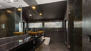 Un baño moderno con un espejo grande, encimera negra y tres lavamanos con detalles dorados.