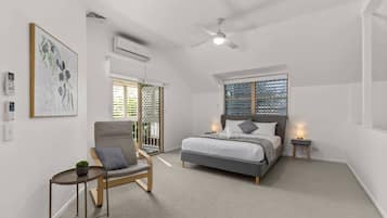 A bedroom with a bed, a chair, a bedside table, a ceiling fan, and a window with blinds.