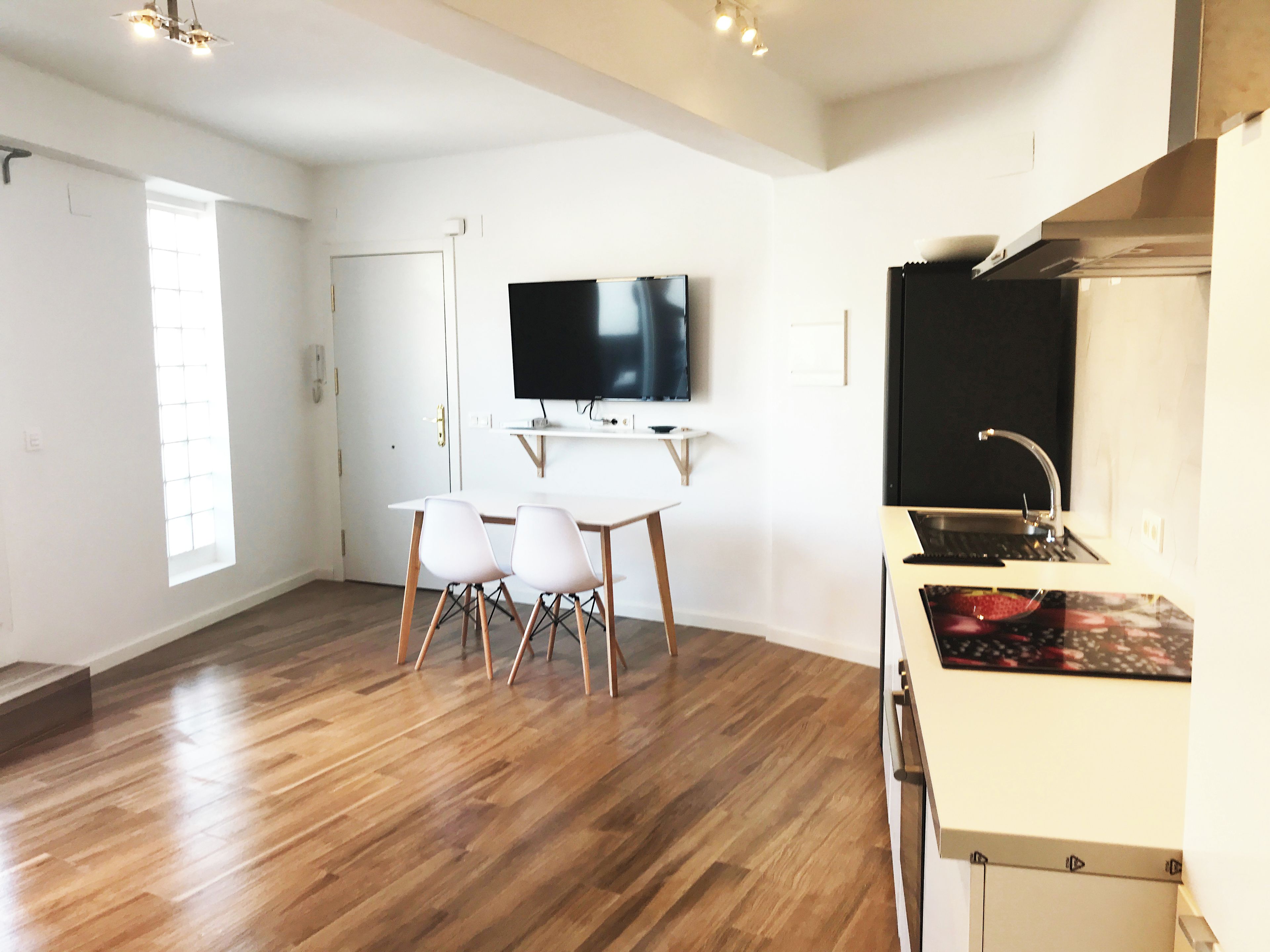 A modern kitchen with a built-in stove, a dining area with a table and chairs, and a flat-screen TV mounted on the wall.