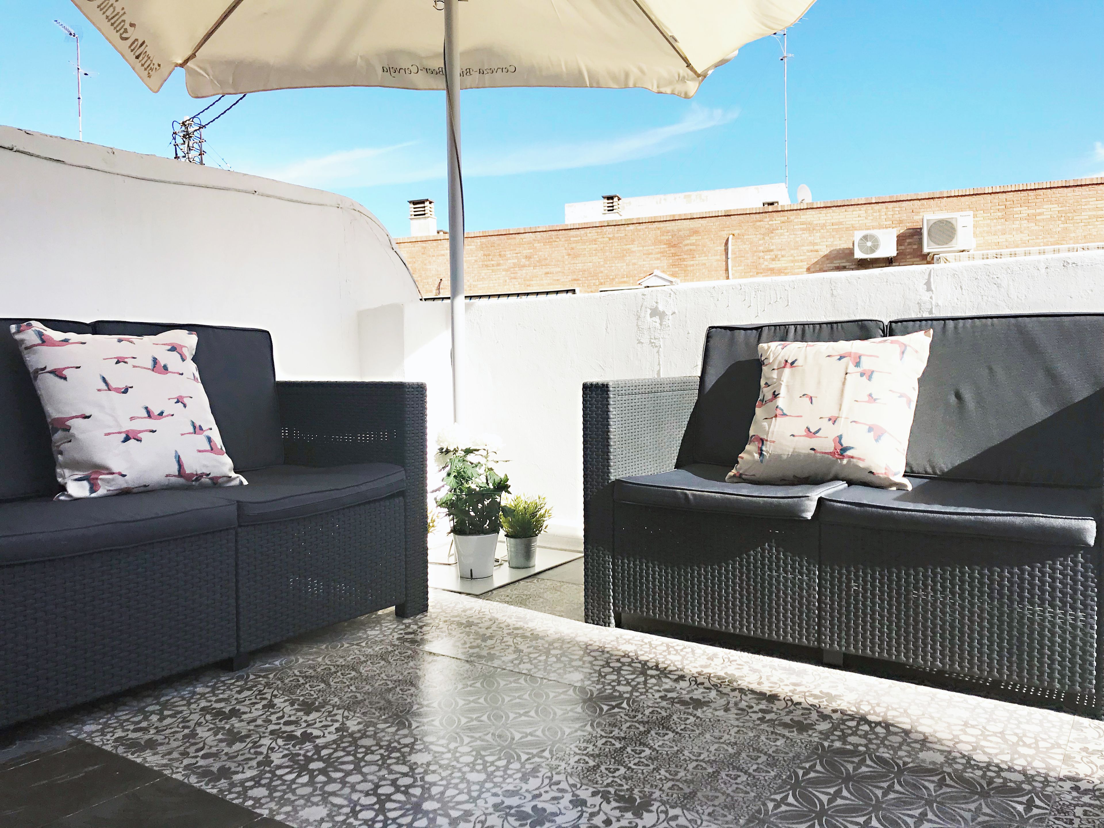 Two dark-colored sofas with patterned pillows, a small potted plant, and a tiled floor with a geometric pattern.