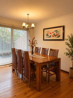 A dining area with a wooden table and chairs, a chandelier, a framed painting, and a potted plant. - Cozy 3-Bedroom Home with Parking & Garden (Doncaster)