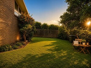 A backyard with a wooden fence, a lawn, and a table with chairs. - Cozy 3-Bedroom Home with Parking & Garden (Doncaster)