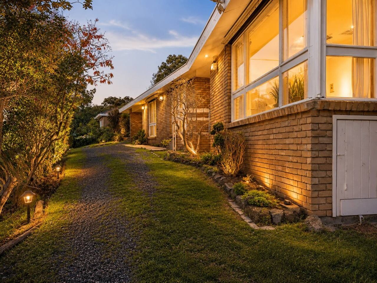 A residential property with a paved driveway, a brick exterior, and a well-lit entrance.