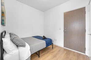 A small, single-bed room with a wooden floor, a white wall, and a wooden door. - *2 Bed Condo* Near UofT/Rogers/Scotia/Hospital/Gym (Toronto)