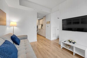 Un saló modern amb un sofà, una televisió i una cuina al fons.