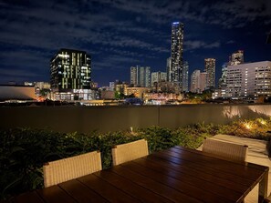 An outdoor dining area with a view of a city skyline at night. - Central Fortitude Valley Stay | 1 Bed, 1 Bath (Fortitude Valley)