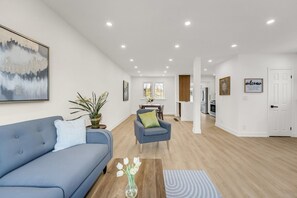 Een moderne woonkamer met een blauwe bank, een salontafel met een bloevas en een eethoek met een tafel en stoelen.