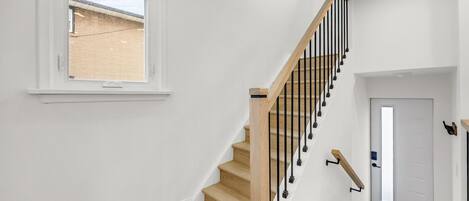 A staircase with wooden steps and black balusters, leading to a landing with a door and a window overlooking a brick building.