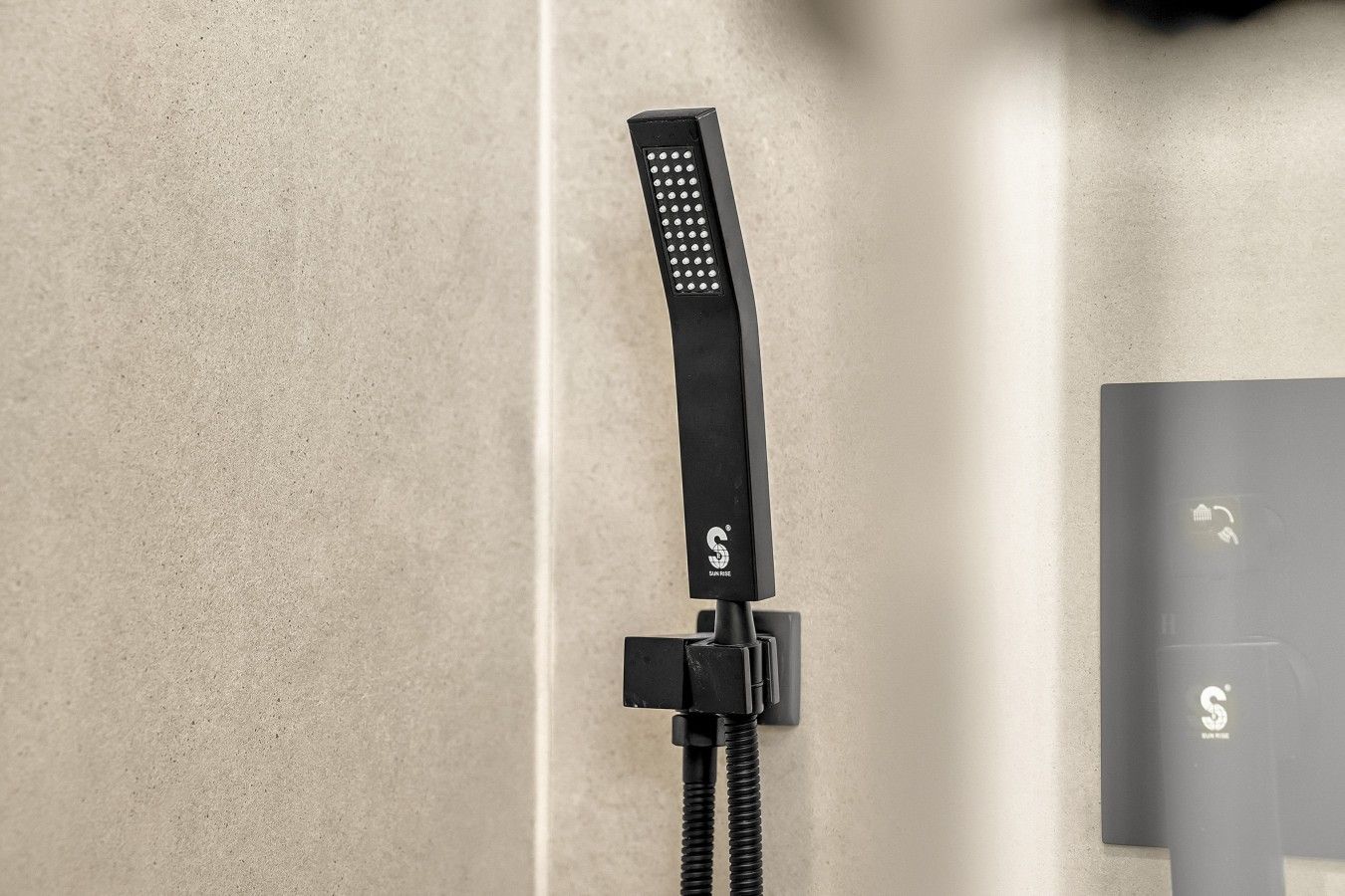 Eine schwarze Handbrause mit Bedienfeld, verbunden mit einem an der Wand befestigten Schlauch.