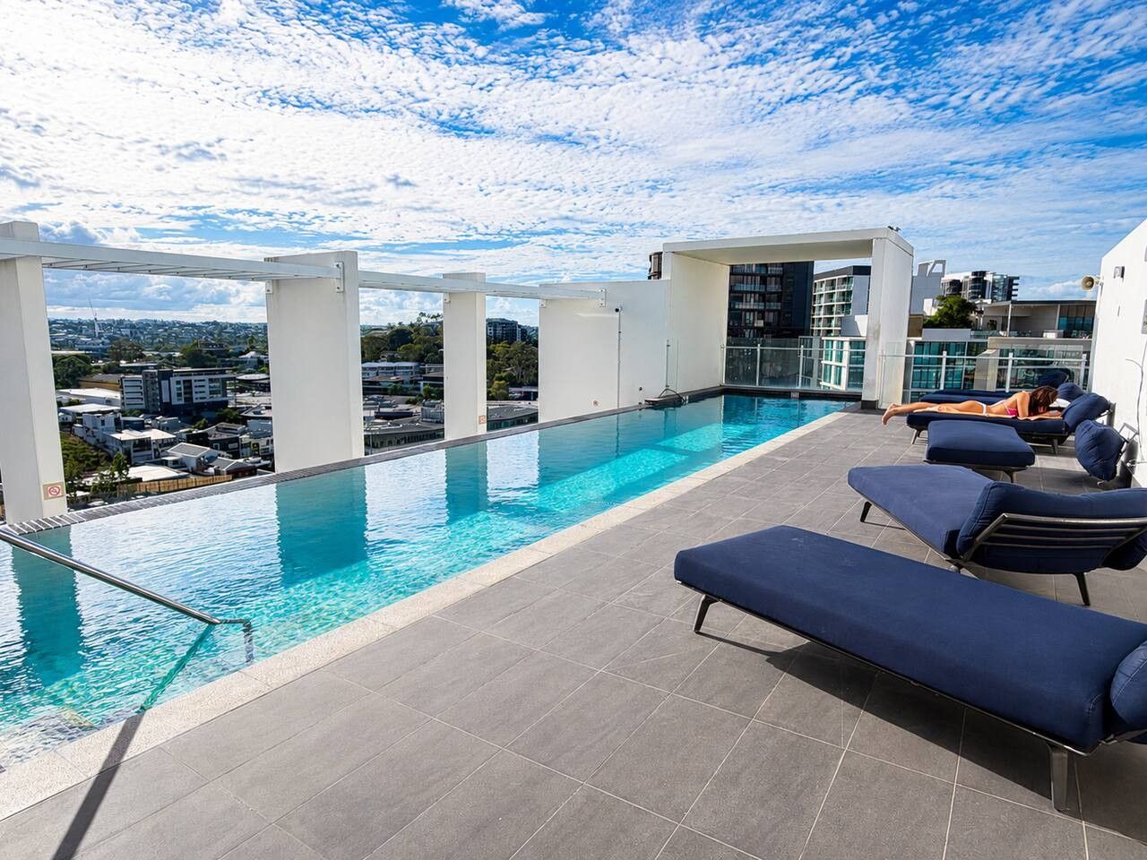 A rooftop pool with clear blue water, surrounded by lounge chairs and a view of the cityscape.