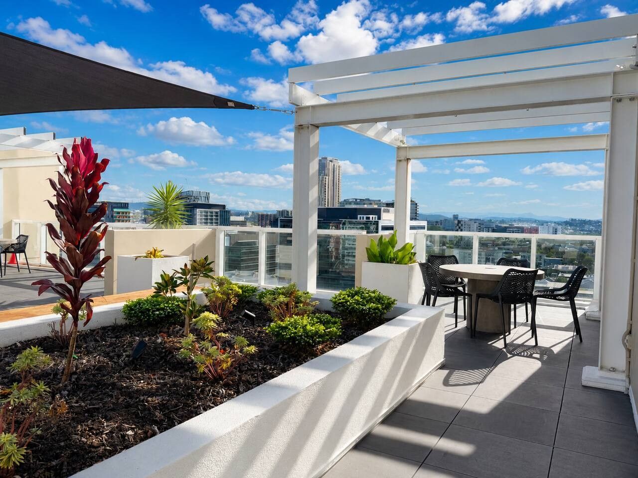 Une terrasse sur le toit agrémentée d’une pergola blanche, d’une table à manger avec des chaises et de diverses plantes.