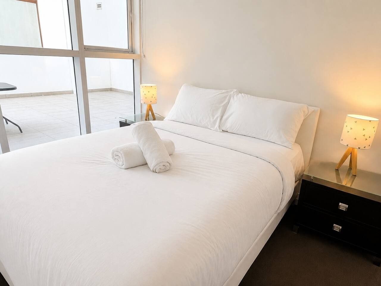 A hotel room with a large bed, two bedside lamps, and a view through a window.