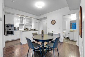 Een moderne keuken met witte kastjes, een eettafel met vier stoelen en een klok aan de muur.