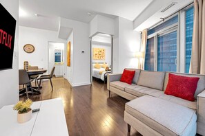 A modern living room with a sofa, a dining area with chairs, a clock, and a bed with a nightstand. - *10/10 Location* 2 BR Downtown Condo with GYM (Toronto)