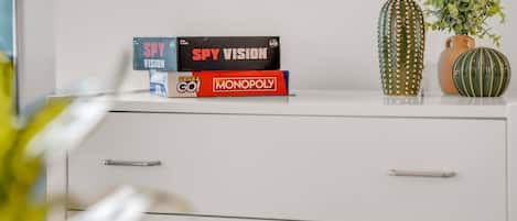 Un escritorio blanco con tres juegos de mesa: Spy Vision, Monopoly y un tercer juego. Hay dos jarrones decorativos con plantas sobre el escritorio.