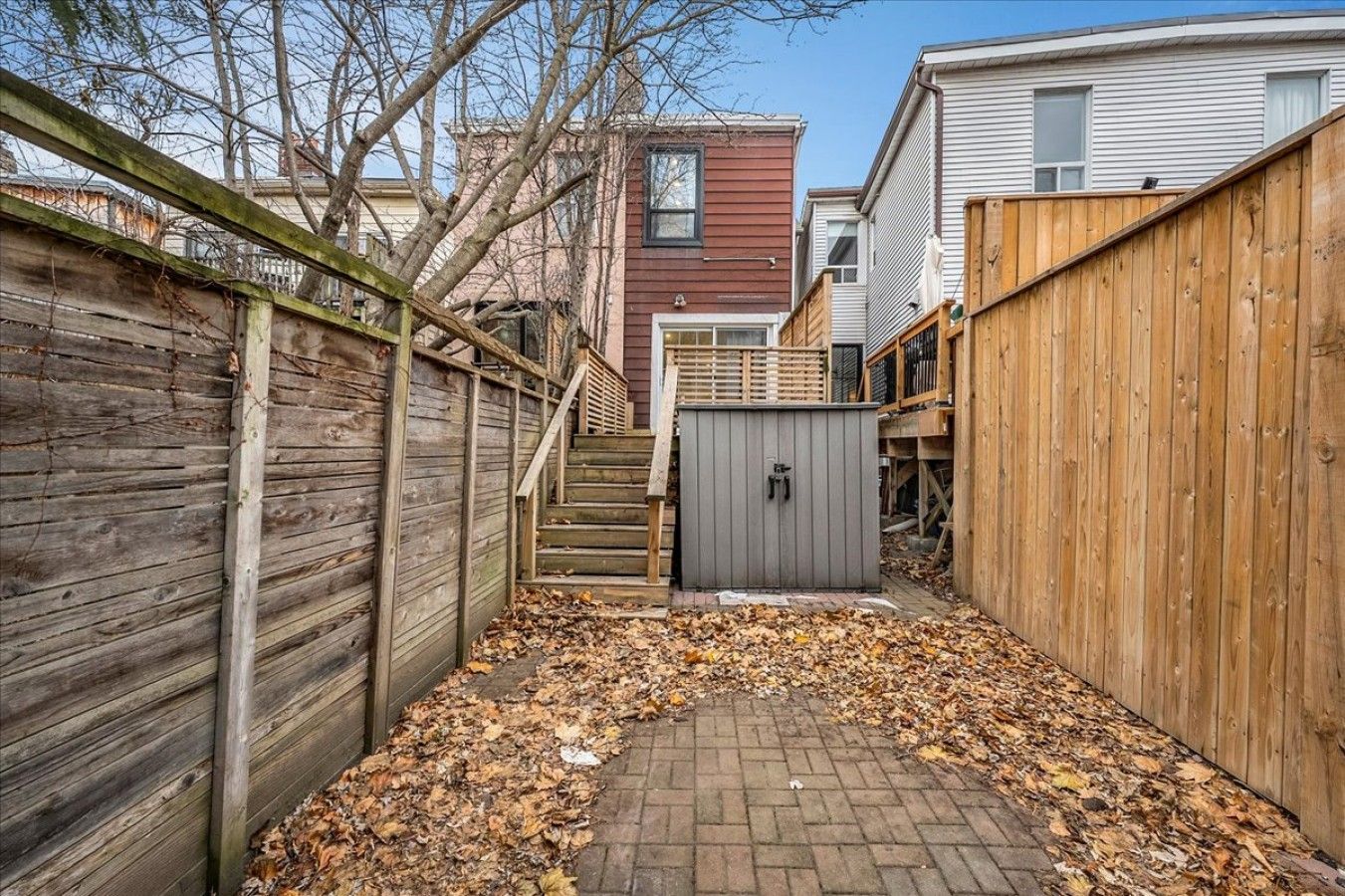 A backyard with a wooden fence, a brick pathway, and a shed.