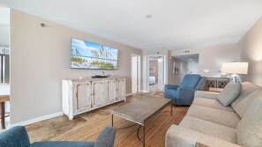 A living room with a flat-screen TV, a cabinet, a sofa, and a coffee table. - Gorgeous Beachfront 1BR at Phoenix East (Orange Beach)