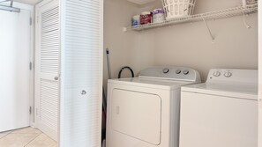 A laundry area with two front-loading washers, a drying rack, and a storage shelf with cleaning supplies. - Gorgeous Beachfront 1BR at Phoenix East (Orange Beach)