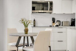 Une cuisine moderne avec des meubles blancs, un four à micro-ondes, une machine à café et un vase rempli de fleurs placé sur une table ronde.